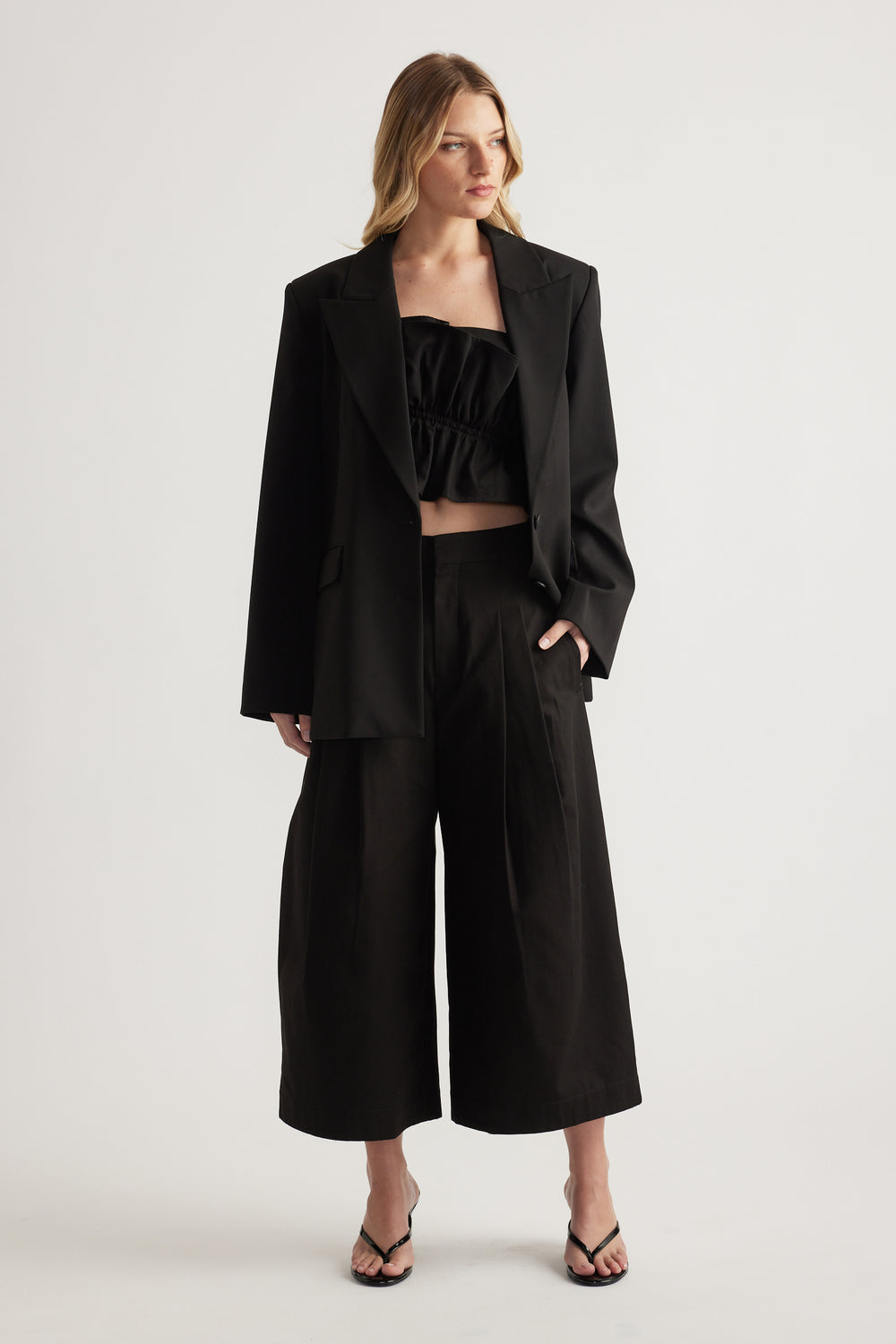 Woman wearing a black blazer with a cropped top, wide leg crop pants and strappy sandals