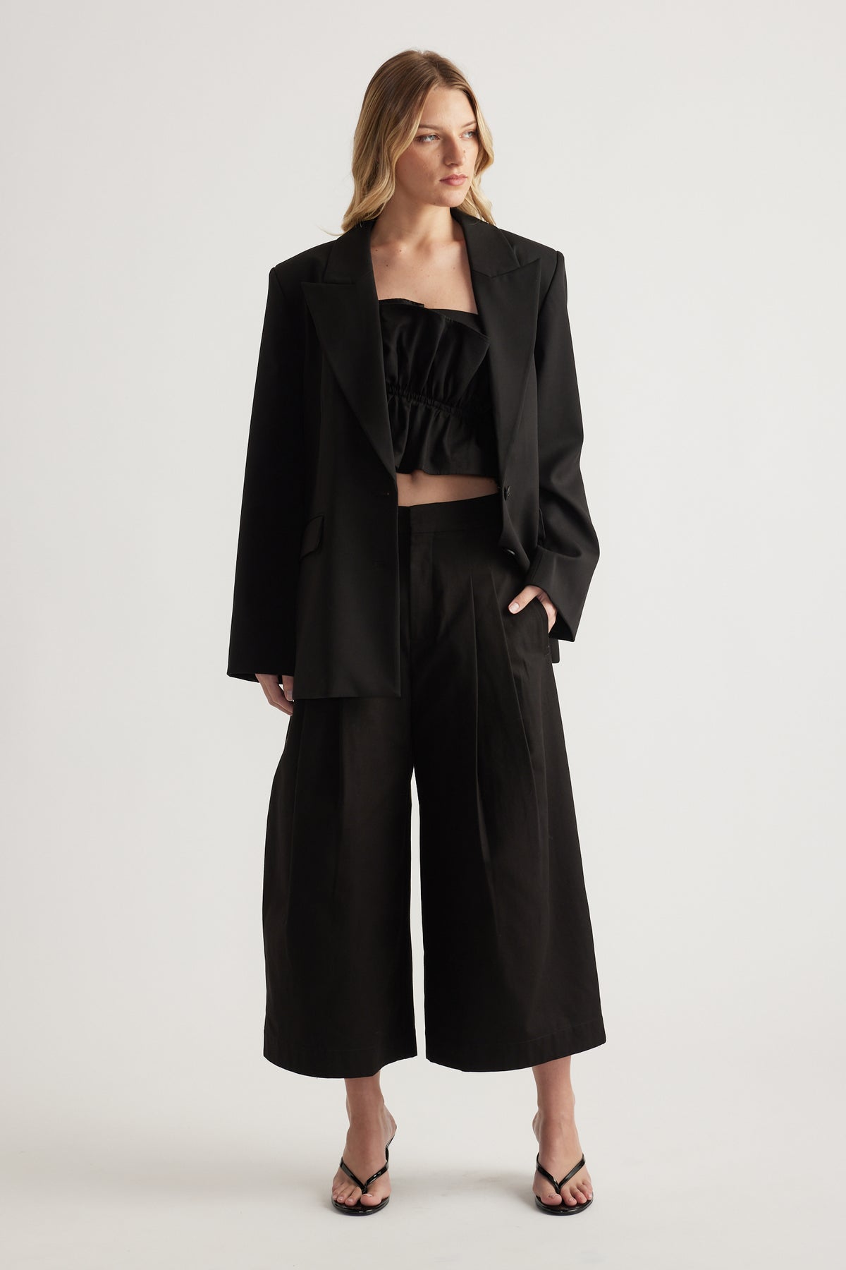 Woman wearing a black blazer with a cropped top, wide leg crop pants and strappy sandals