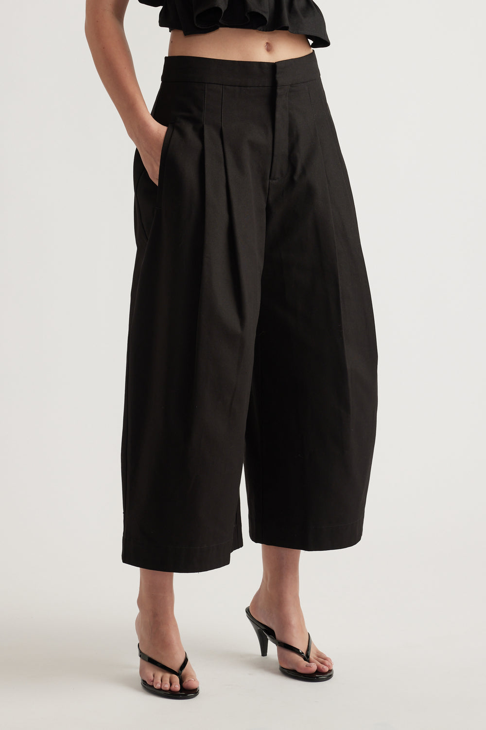 Woman wearing black high rise pleated cropped wide leg pants with black heeled sandals