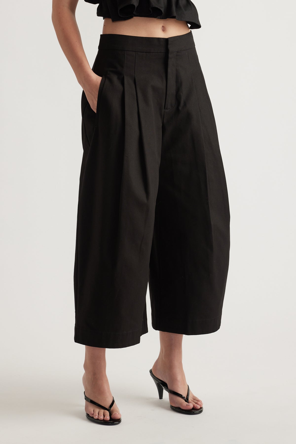 Woman wearing black high rise pleated cropped wide leg pants with black heeled sandals