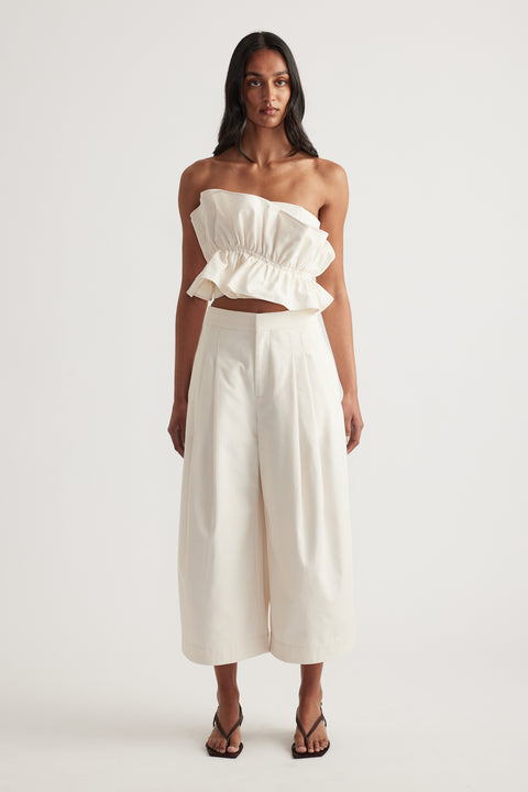 Woman in a cream strapless ruffle top and cropped wide leg pants with black sandals