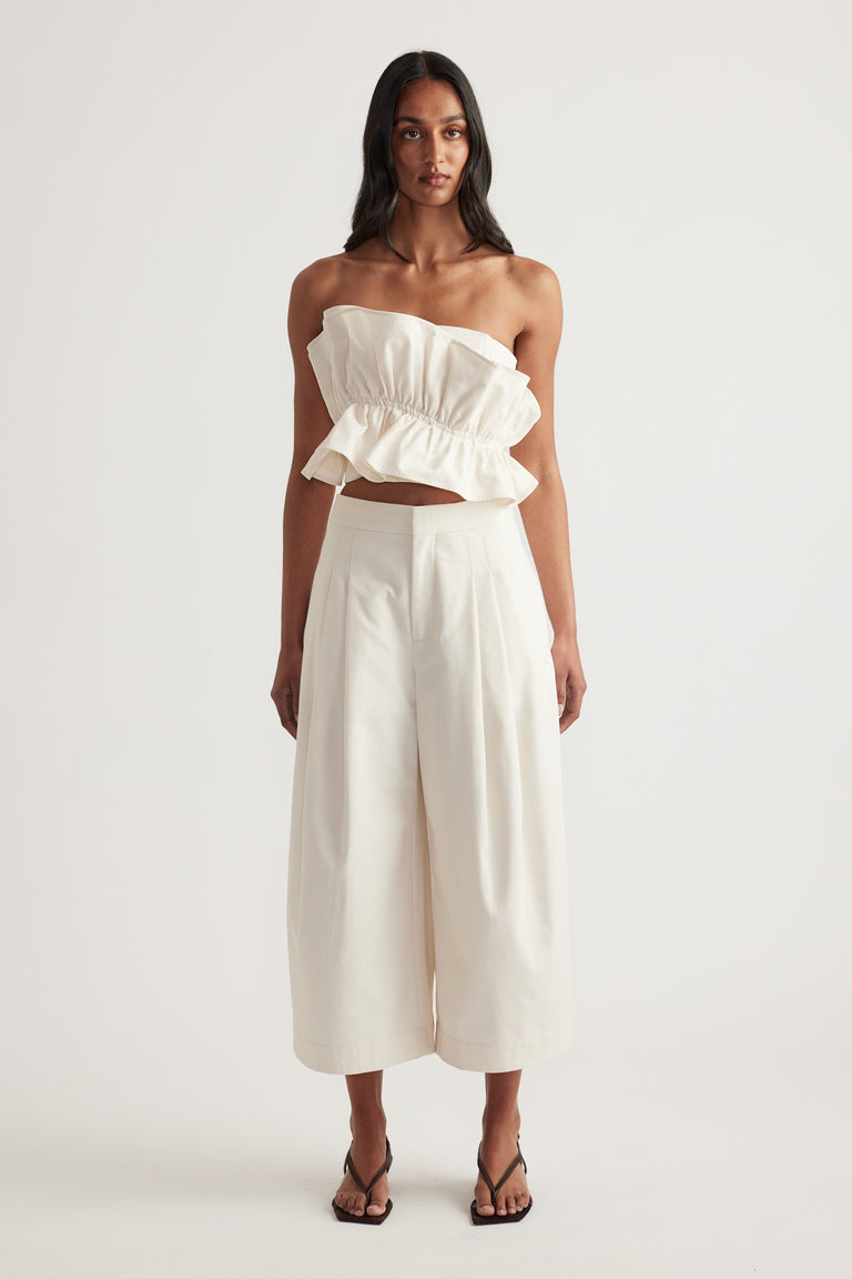 Woman in a cream strapless ruffle top and cropped wide leg pants with black sandals