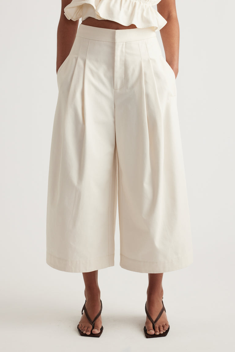 Woman wearing white high rise pleated cropped wide leg pants with a ruffle top and black strappy sandals