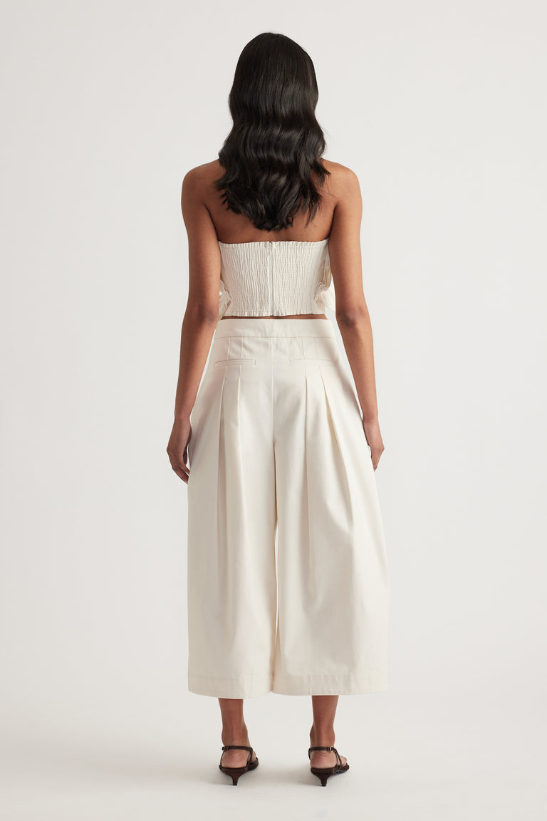 Back view of a woman wearing a cream strapless top with pleated wide leg pants and black heels