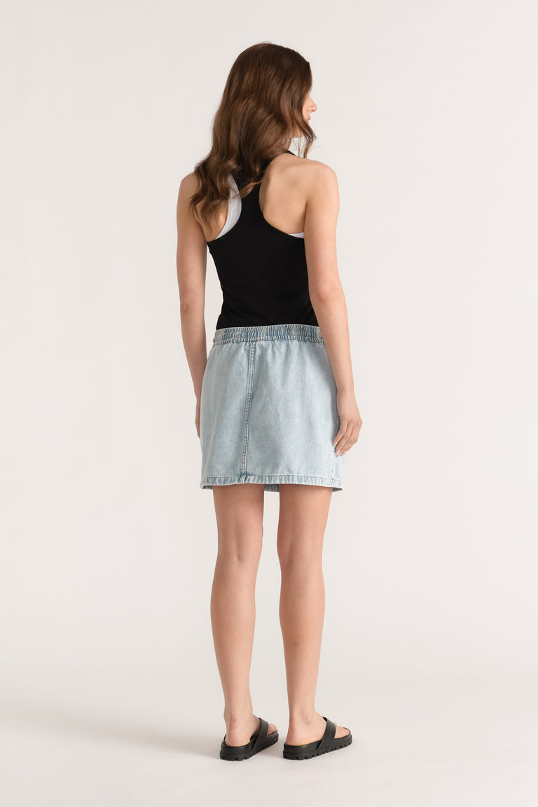 Model wearing a light wash denim mini skirt with an elastic waist, black tank top and black sandals