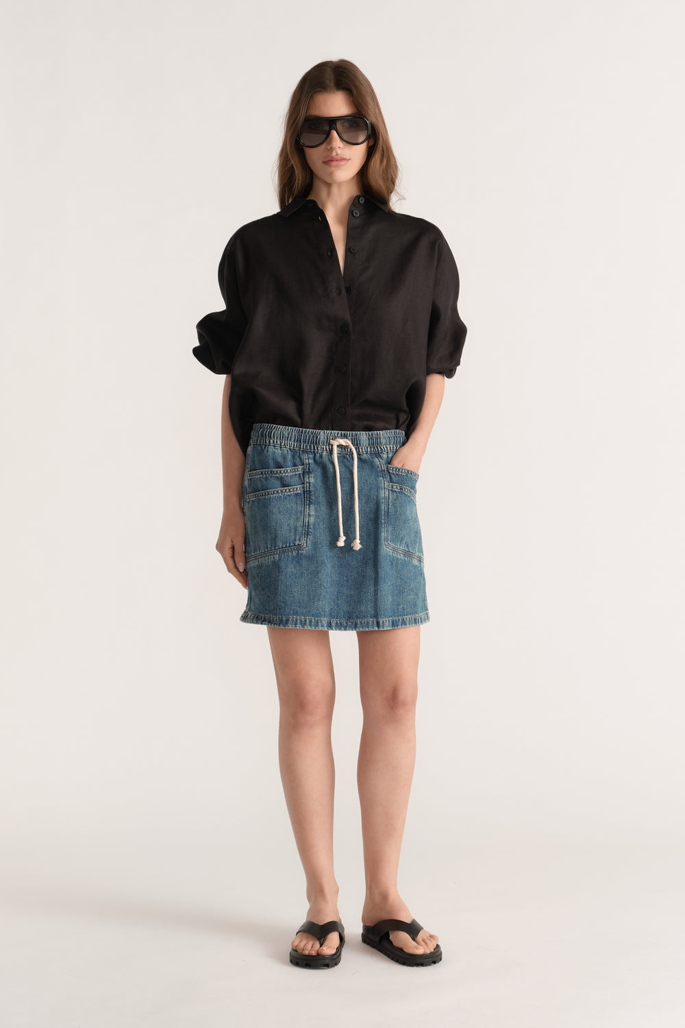 Woman wearing a blue denim mini skirt with an elastic drawstring waist, black shirt and flat sandals