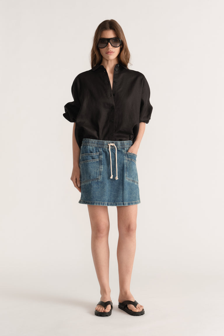 Woman wearing a blue denim mini skirt with an elastic drawstring waist, black shirt and flat sandals