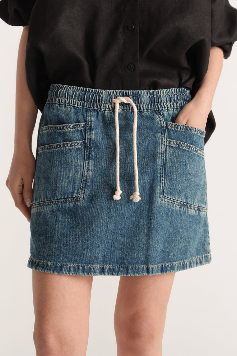 Woman wearing a blue denim mini skirt with an elastic waist, drawstring and front pockets