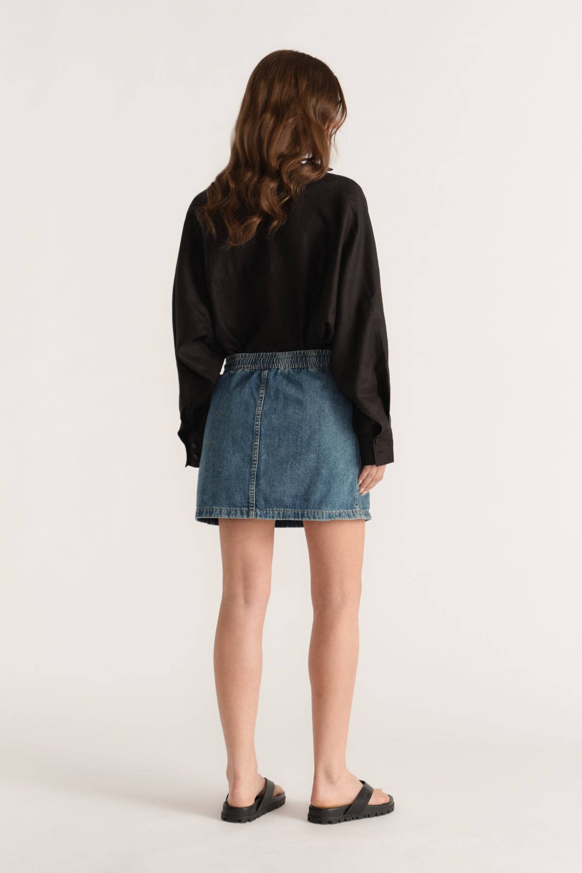 Woman wearing a blue denim mini skirt with a black long sleeve top and flat sandals