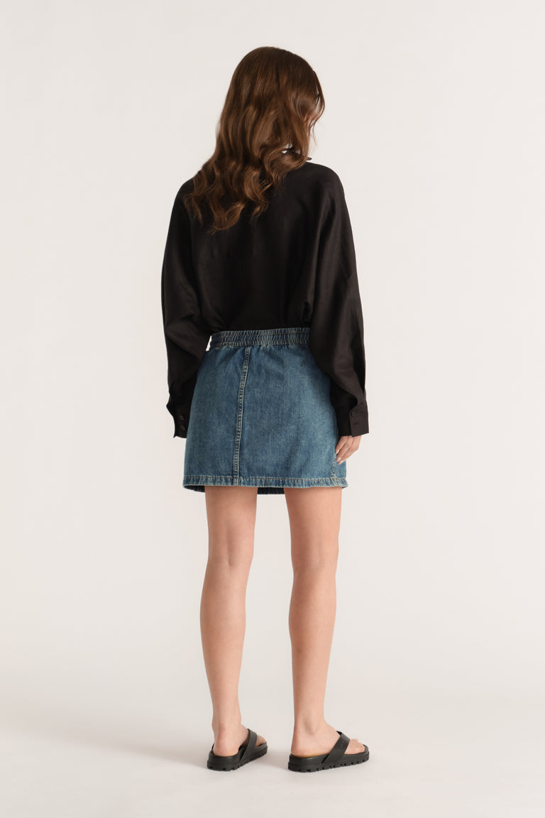 Woman wearing a blue denim mini skirt with a black long sleeve top and flat sandals