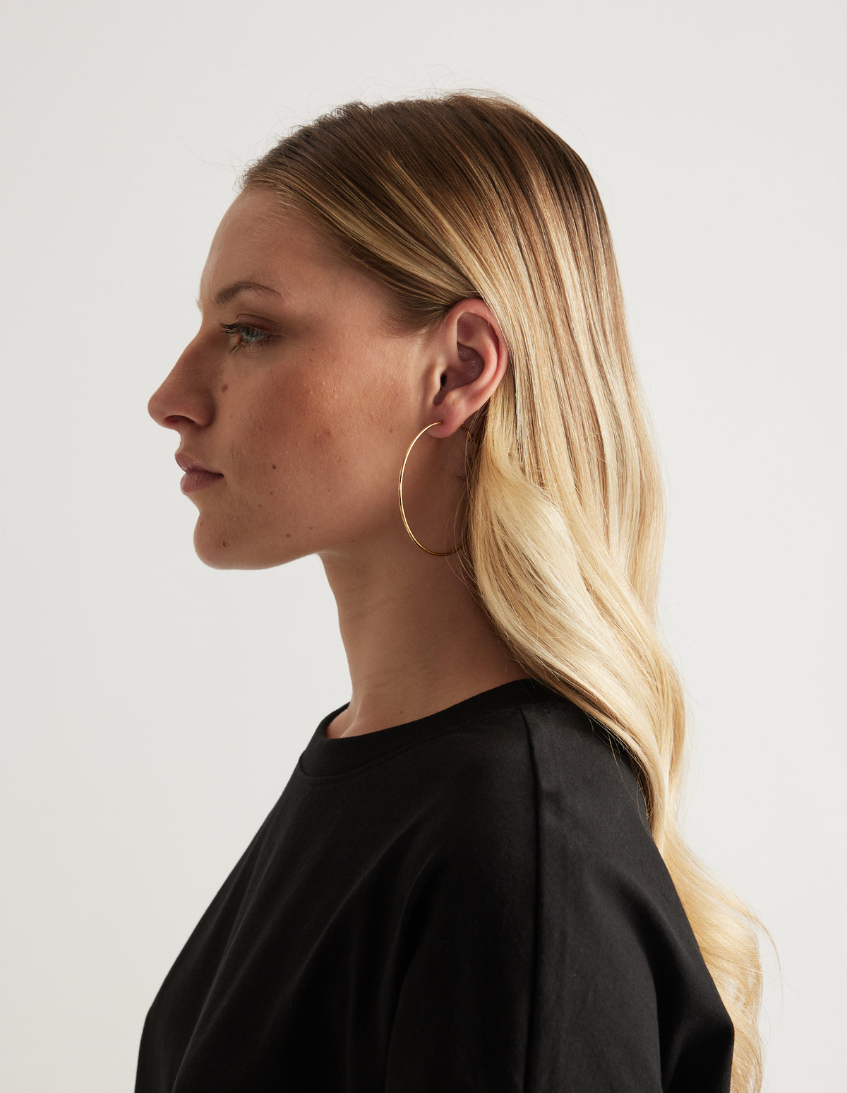 Woman in profile wearing a thin gold hoop earring and black top