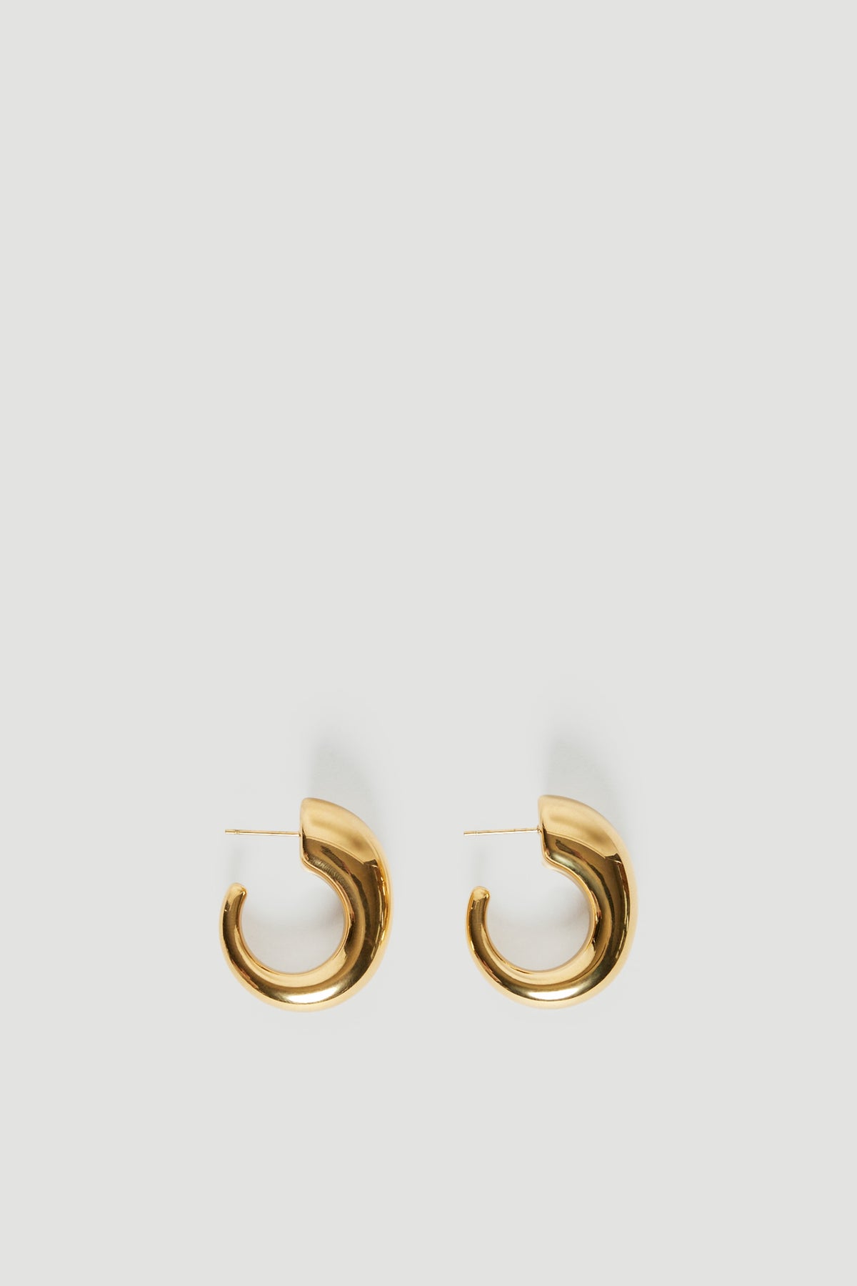 Pair of chunky gold half moon hoop earrings on a light background