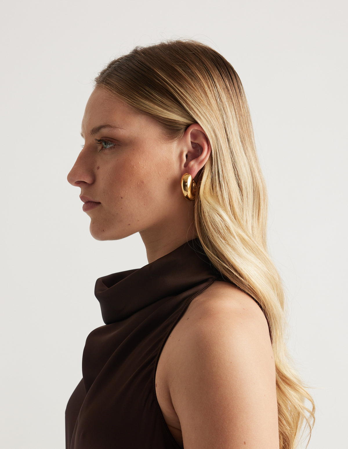 Side profile of a woman wearing a chunky gold hoop earring with a dark brown top