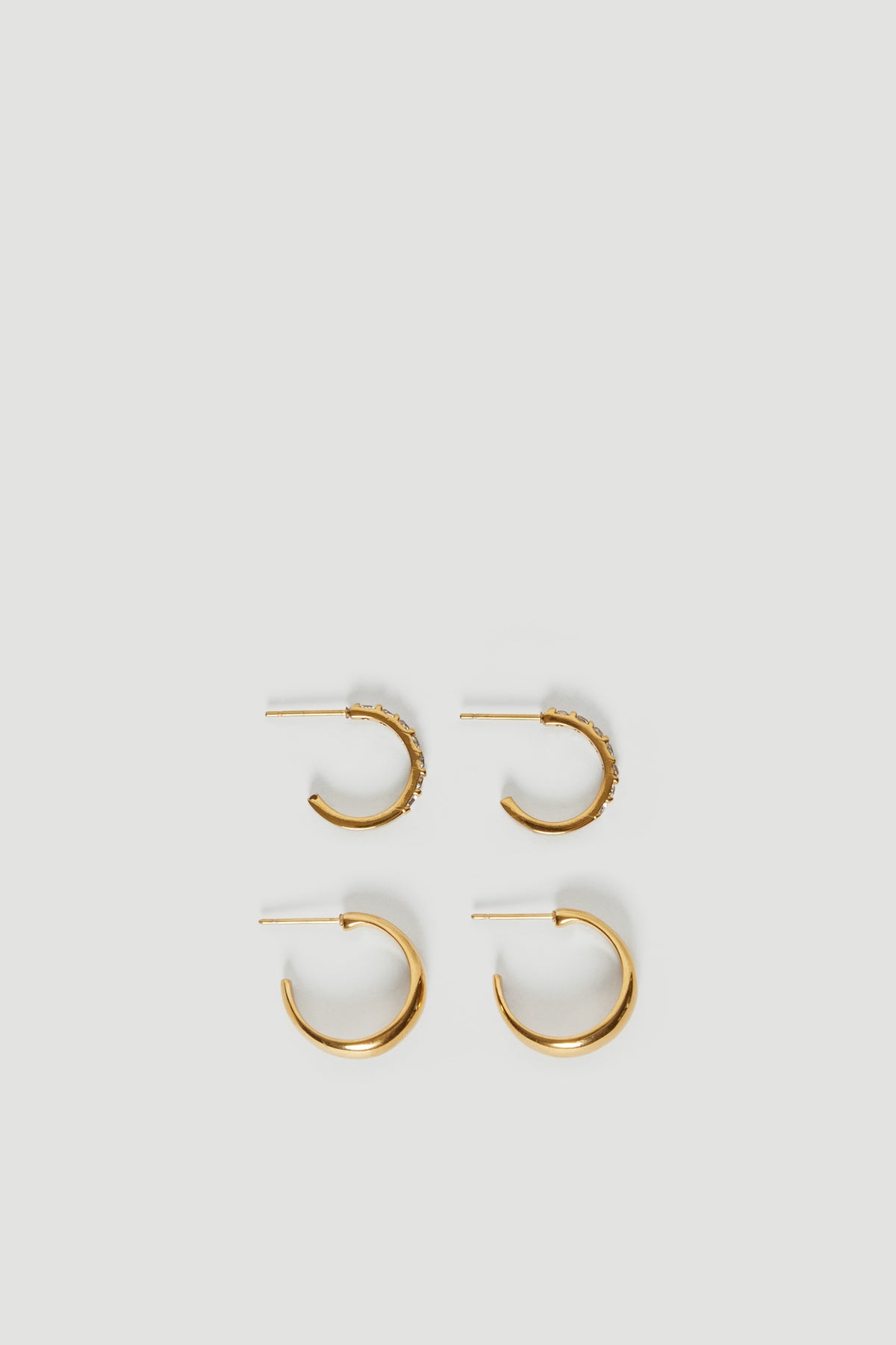 Two pairs of gold hoop earrings arranged on a light background