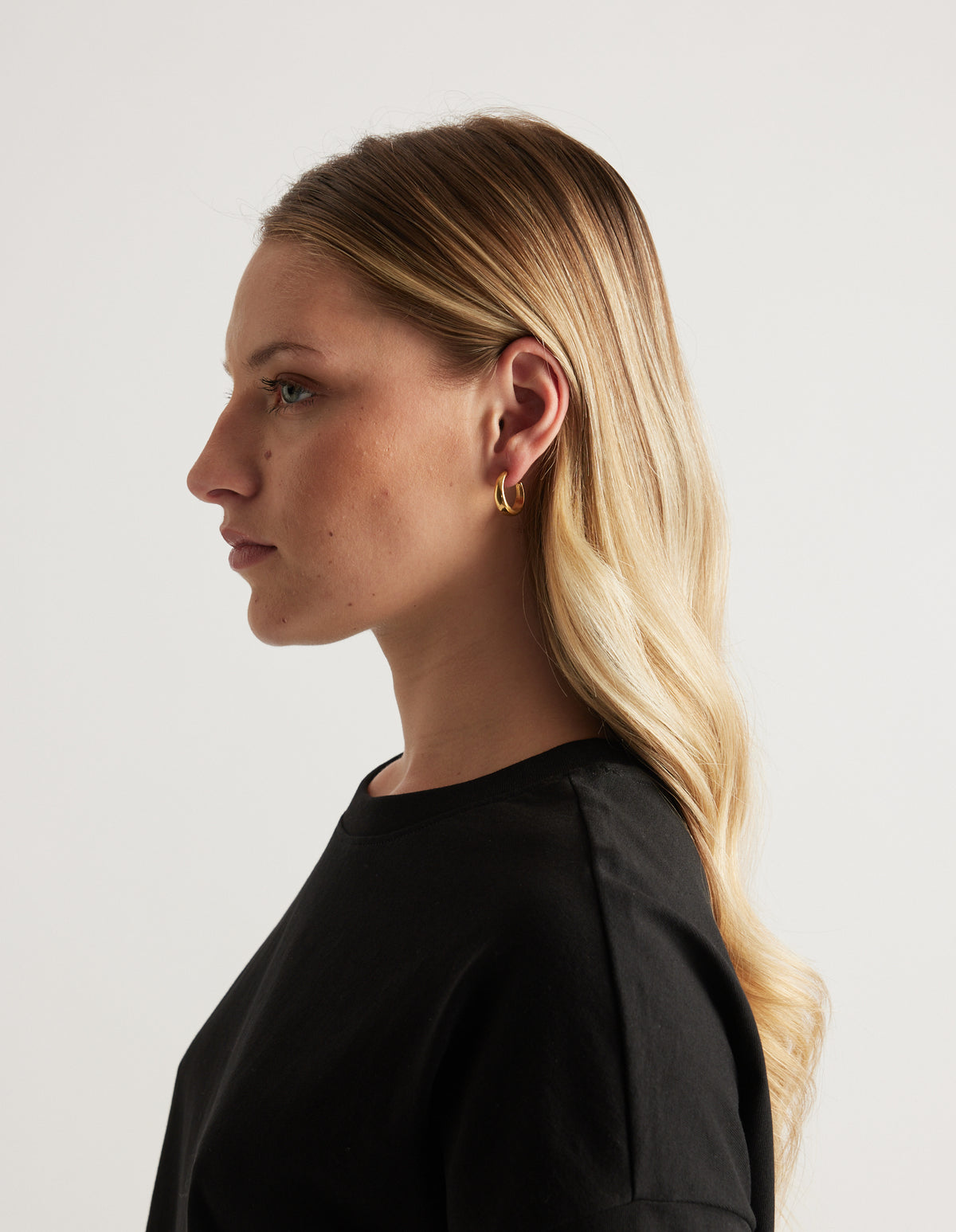 Woman in profile wearing small gold hoop earrings and a black top