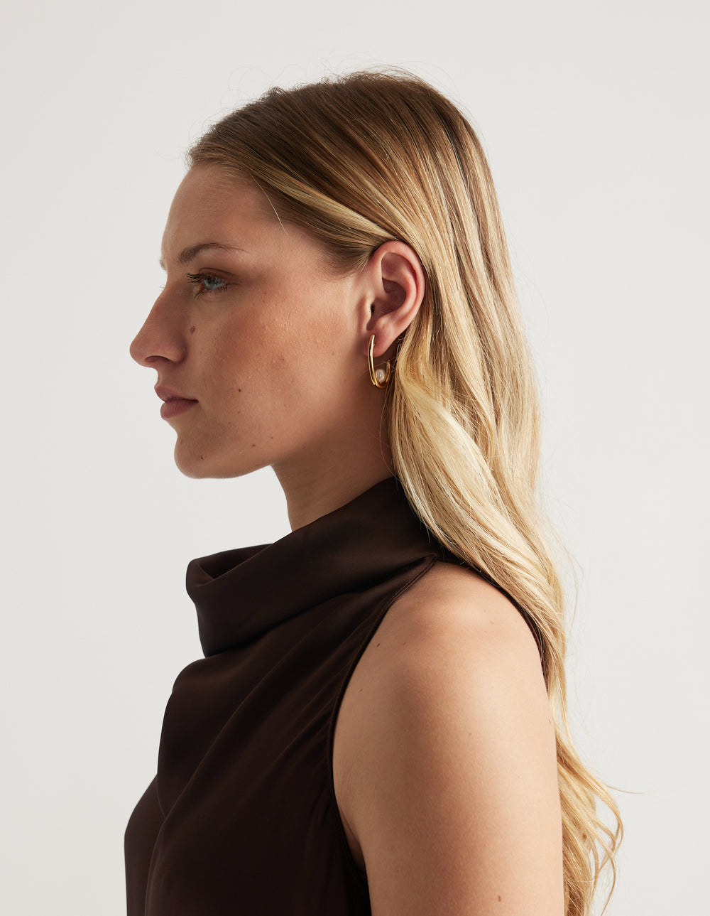 Woman in side profile wearing a gold oval hoop earring