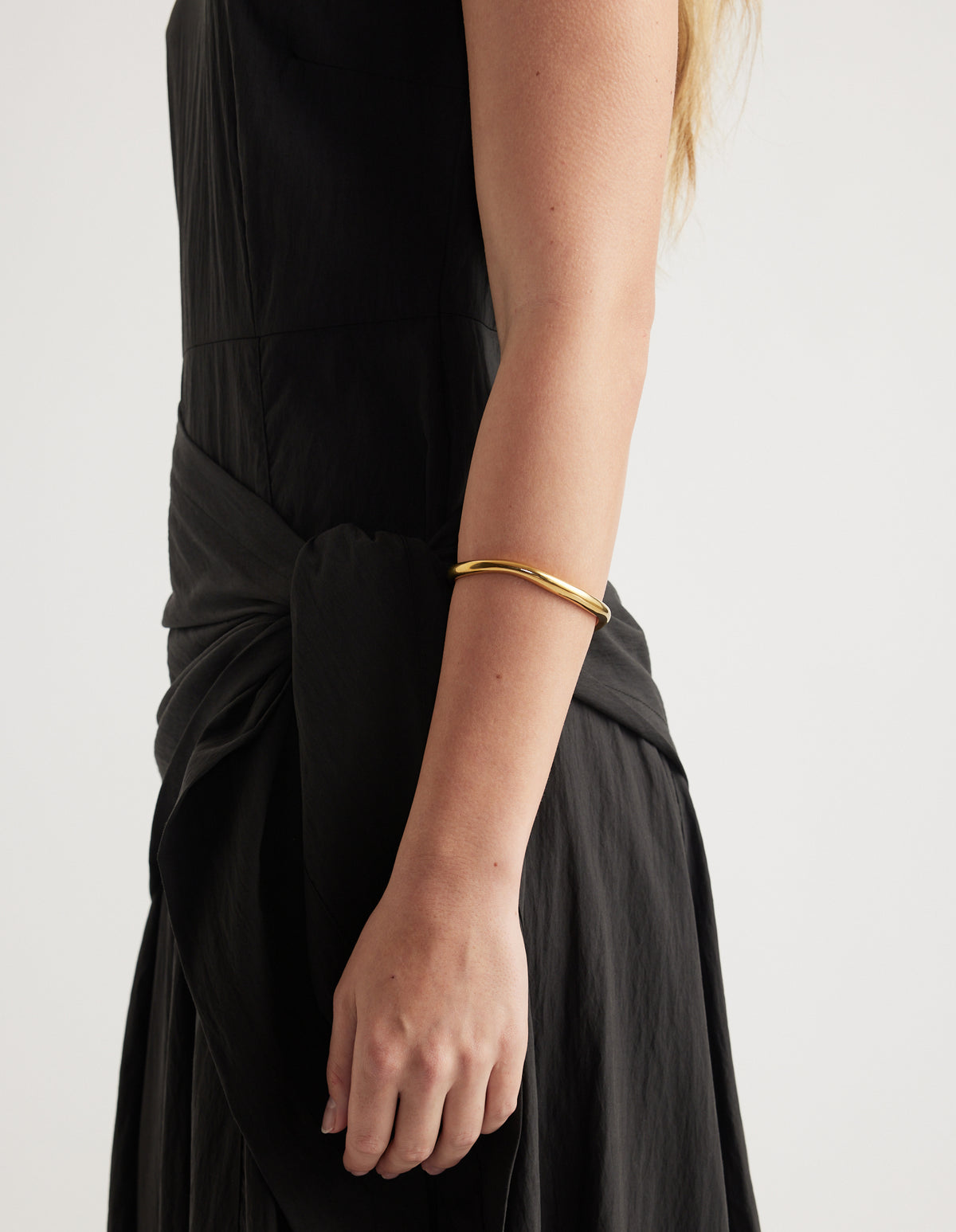Close-up of a woman wearing a slim gold cuff bracelet with a black outfit