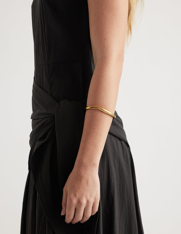 Close-up of a woman wearing a slim gold cuff bracelet with a black outfit