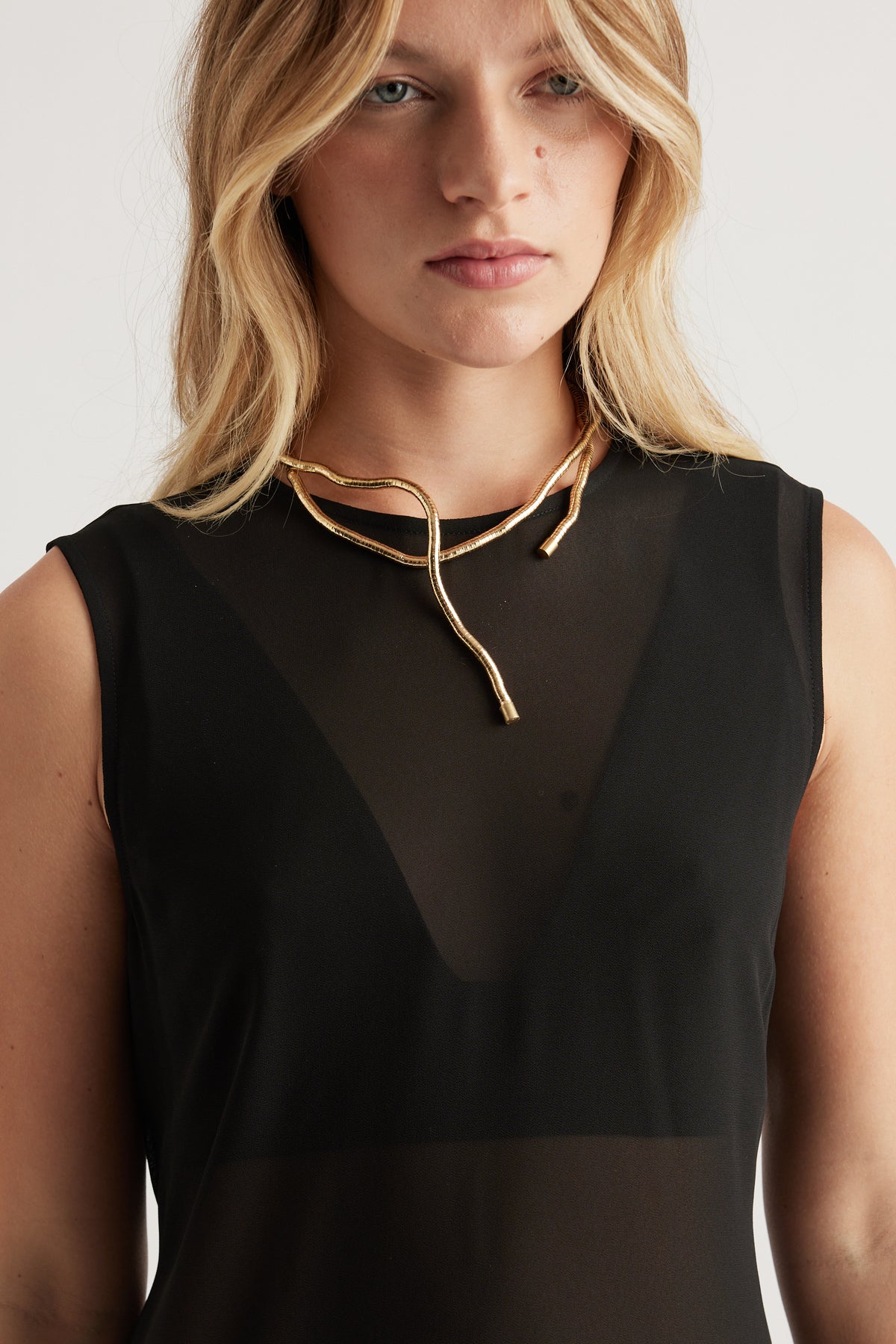 Close-up of woman wearing a sculptural gold wrap necklace paired with a sheer black sleeveless top for a chic look