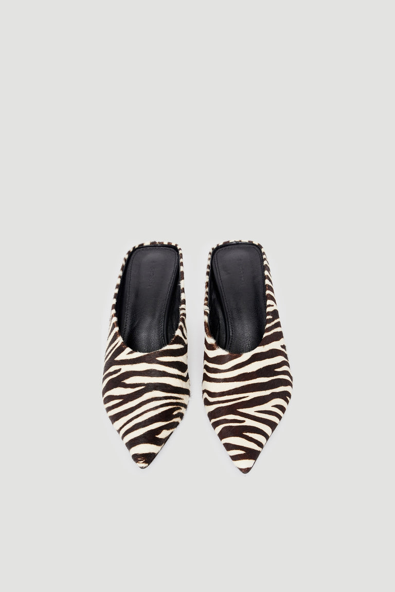 Pair of pointed mule heels with black and white zebra print pony hair upper and black cushioned insole on grey background