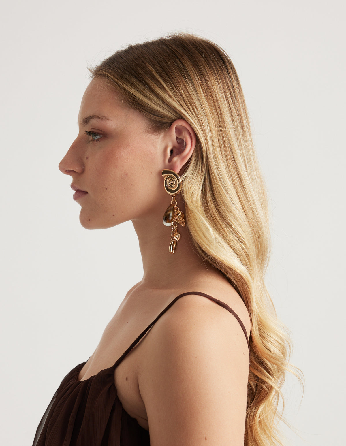 Side profile of a woman wearing a shiny gold shell tassel earring with multiple dangling pendants