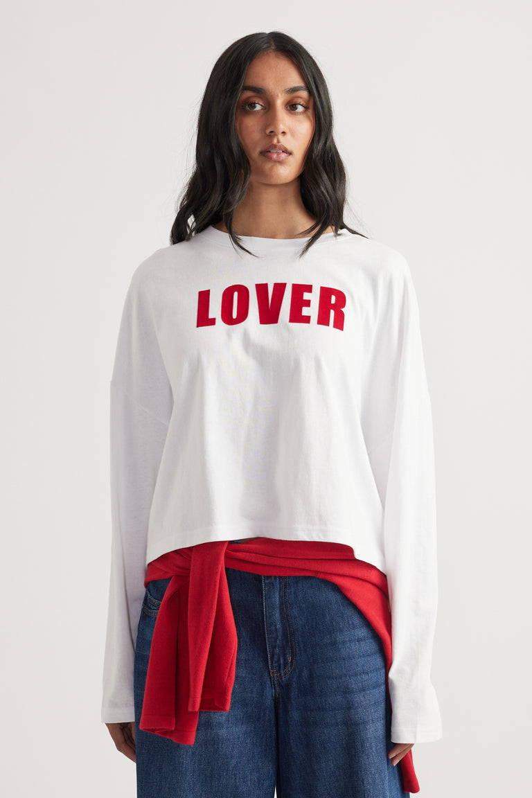 Front view of woman wearing white oversized long sleeve tee with red "LOVER" text and blue denim jeans