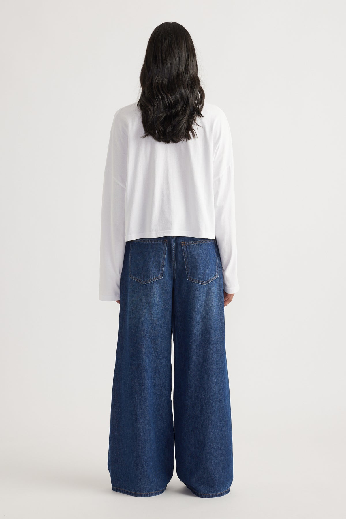 Rear view of woman wearing wide-leg dark blue denim jeans paired with a loose white long sleeve tee