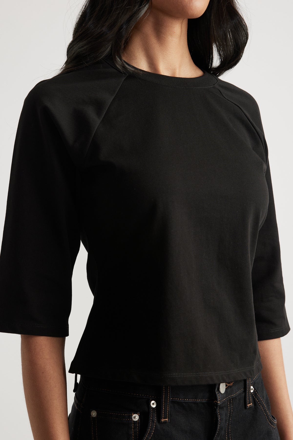 Woman wearing a fitted black crew neck tee with three quarter raglan sleeves and seam detailing