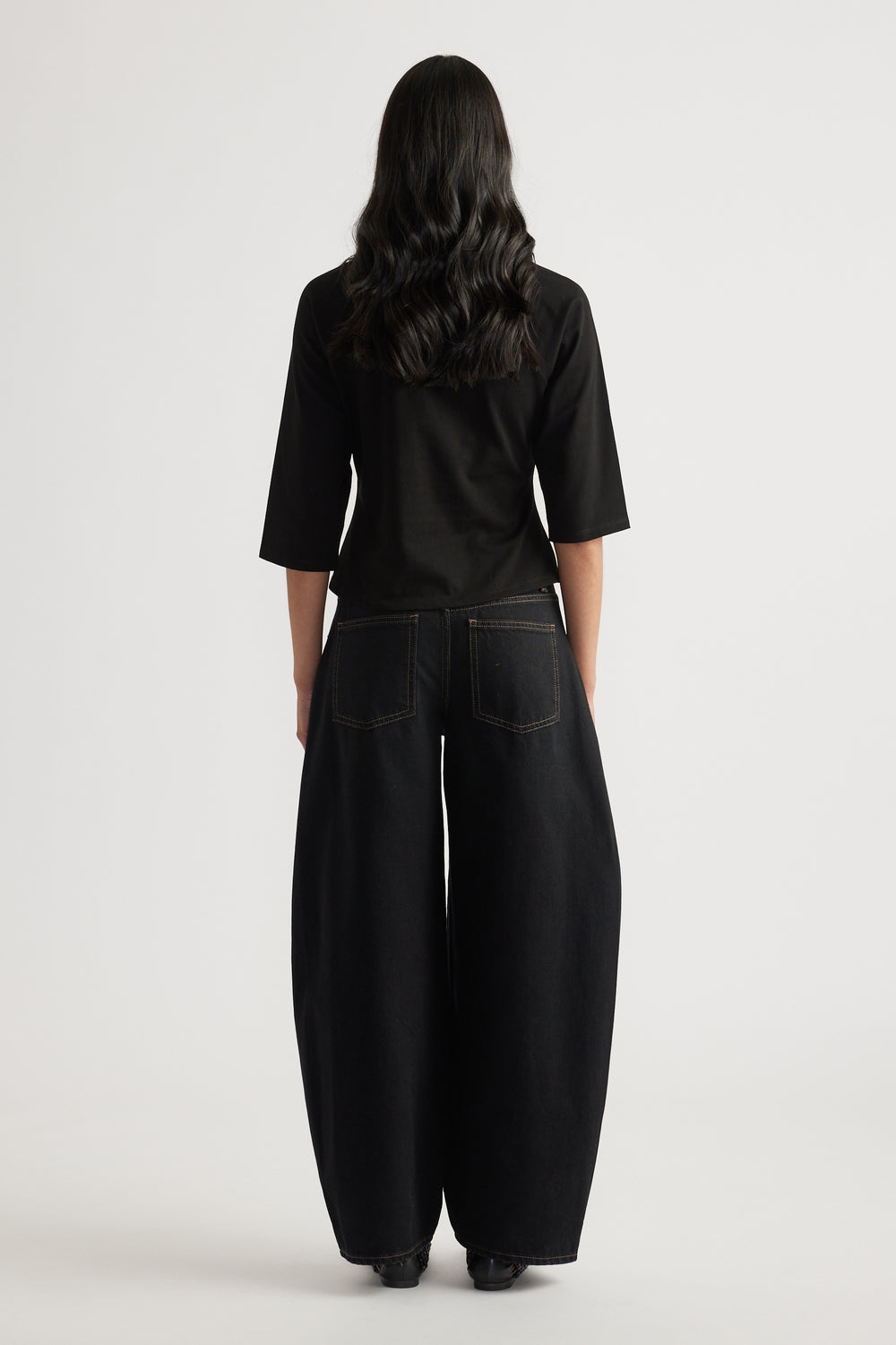 Woman viewed from behind wearing a black three-quarter sleeve tee with black wide-leg jeans