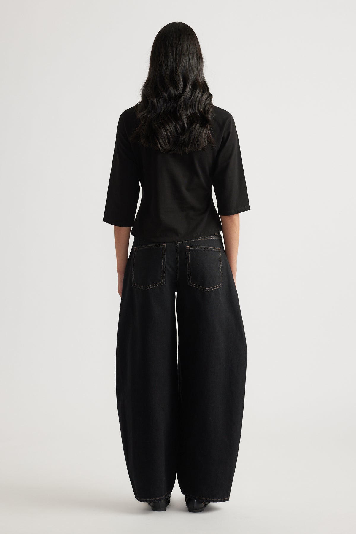 Woman viewed from behind wearing a black three-quarter sleeve tee with black wide-leg jeans