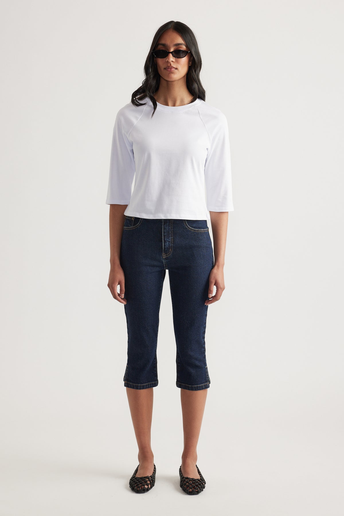 Woman wearing a white fitted three quarter sleeve crew neck tee with dark cropped jeans and sunglasses