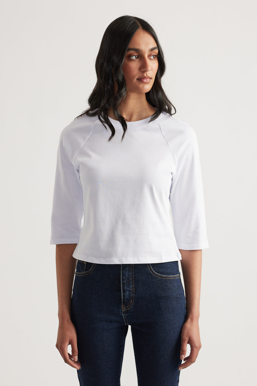 Woman wearing a white three quarter sleeve crew neck tee with dark blue jeans