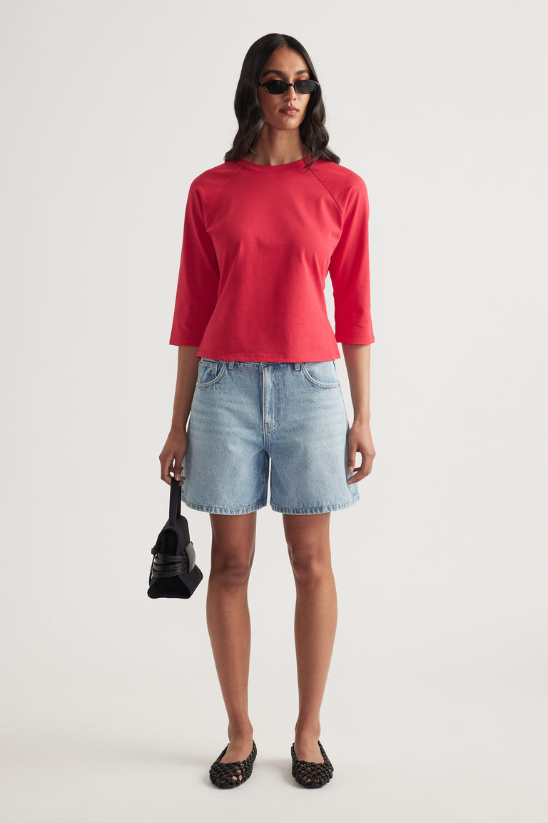 Woman wearing a red fitted three-quarter sleeve tee with denim shorts and sunglasses