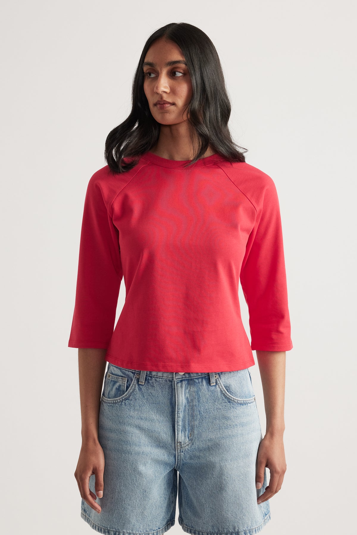 Woman wearing a red fitted three quarter sleeve crew neck tee with denim shorts