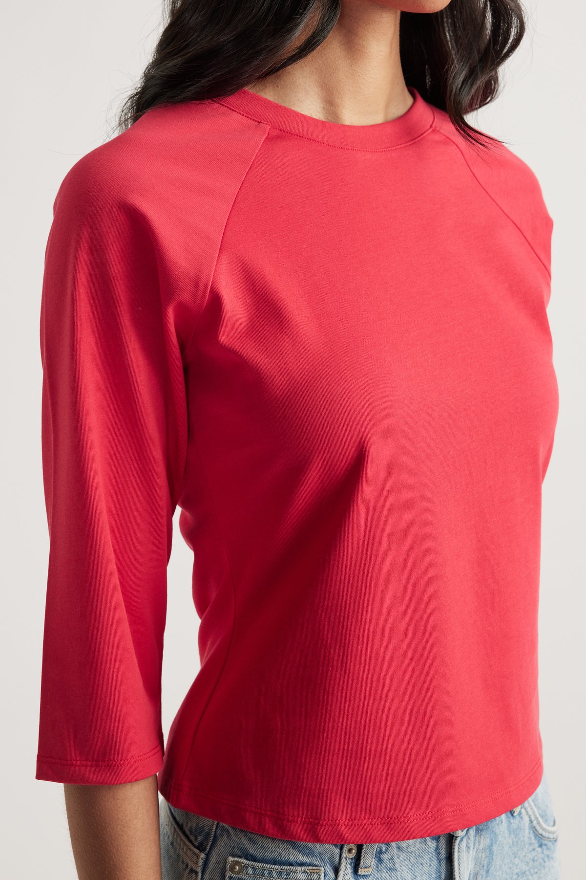 Woman wearing a coral 3/4 sleeve raglan crew neck tee with seam detailing and jeans