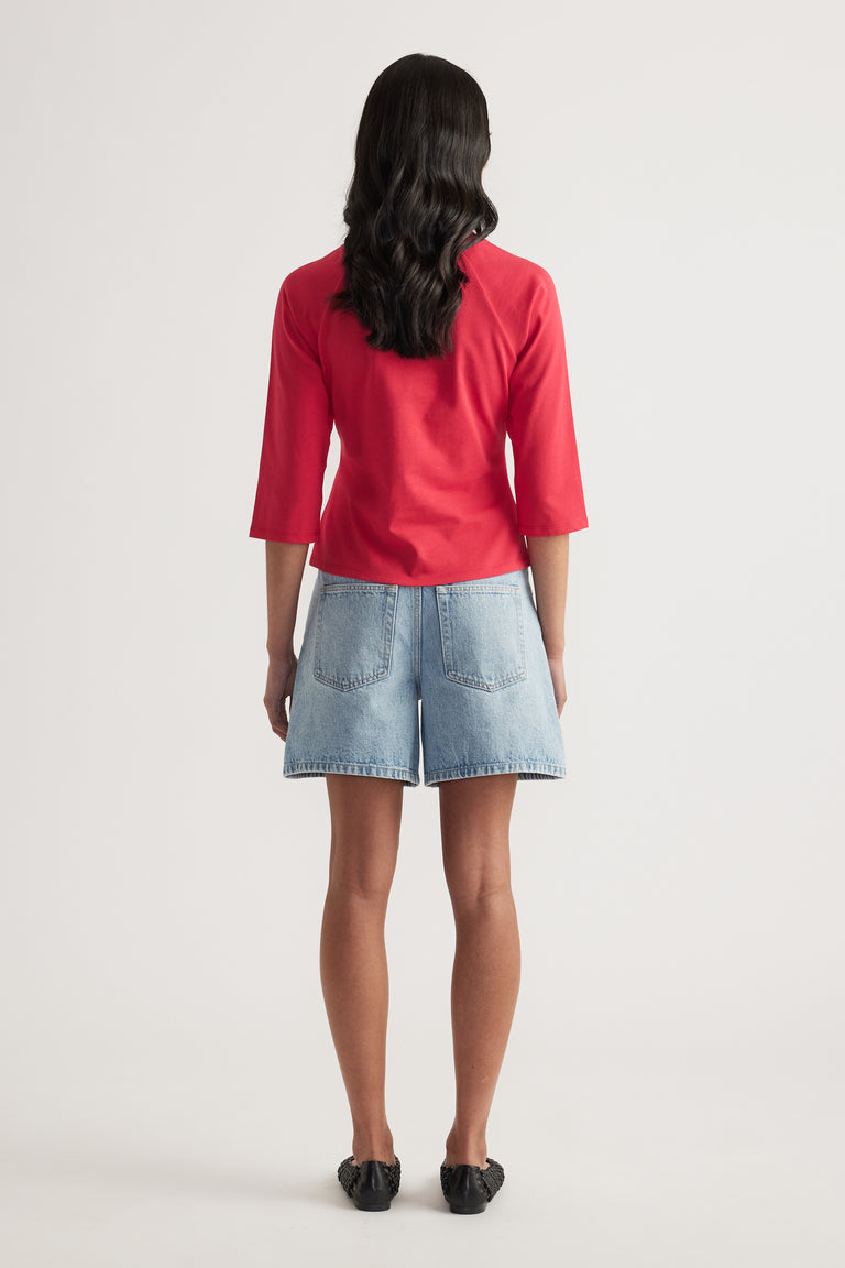 Woman viewed from behind wearing a red three-quarter sleeve tee and light wash denim shorts