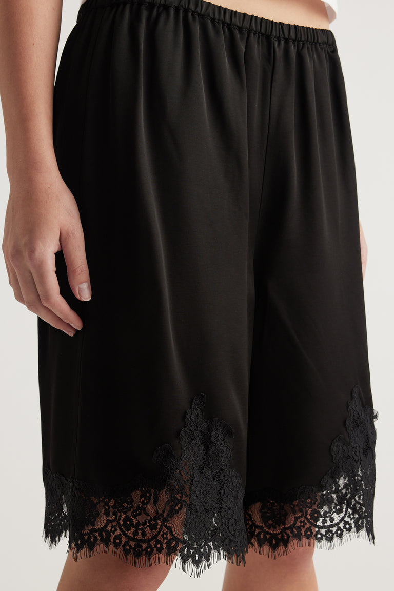 Woman wearing black satin bermuda shorts with delicate lace trim маз 恒一