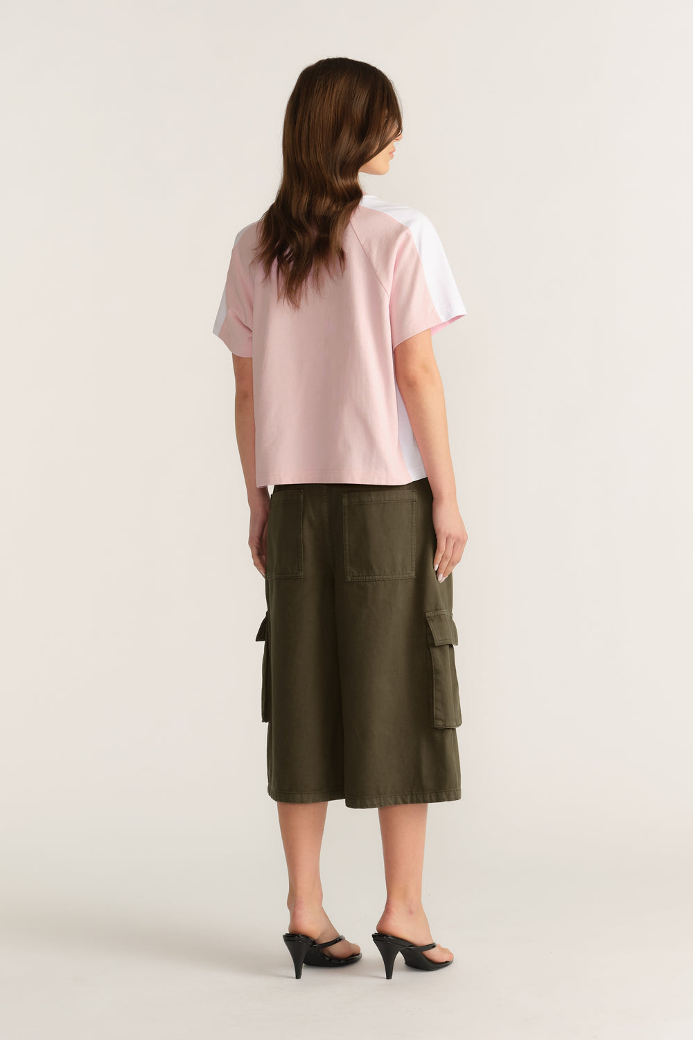 Back view of a woman wearing a pink short sleeve tee with an olive cargo midi skirt and black heels