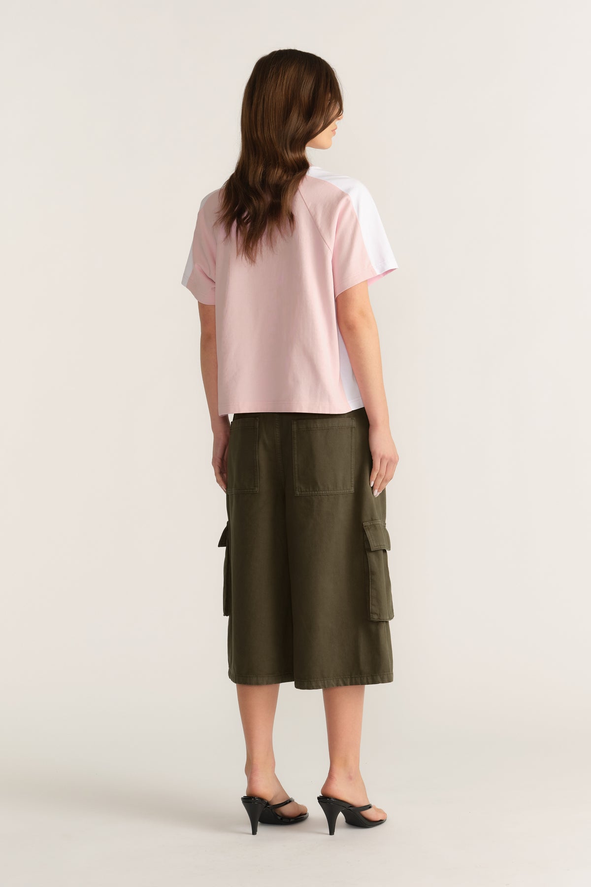 Back view of a woman wearing a pink short sleeve tee with an olive cargo midi skirt and black heels