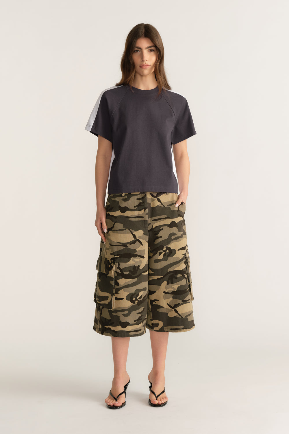 Woman wearing a charcoal short sleeve round neck tee with camouflage cargo shorts and flip flops