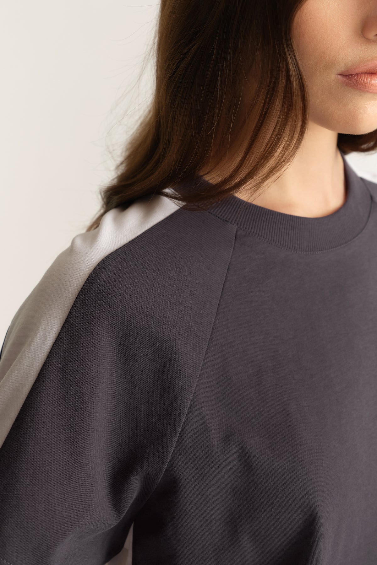Close-up of a woman wearing a charcoal grey crew neck tee with contrasting light shoulder panels