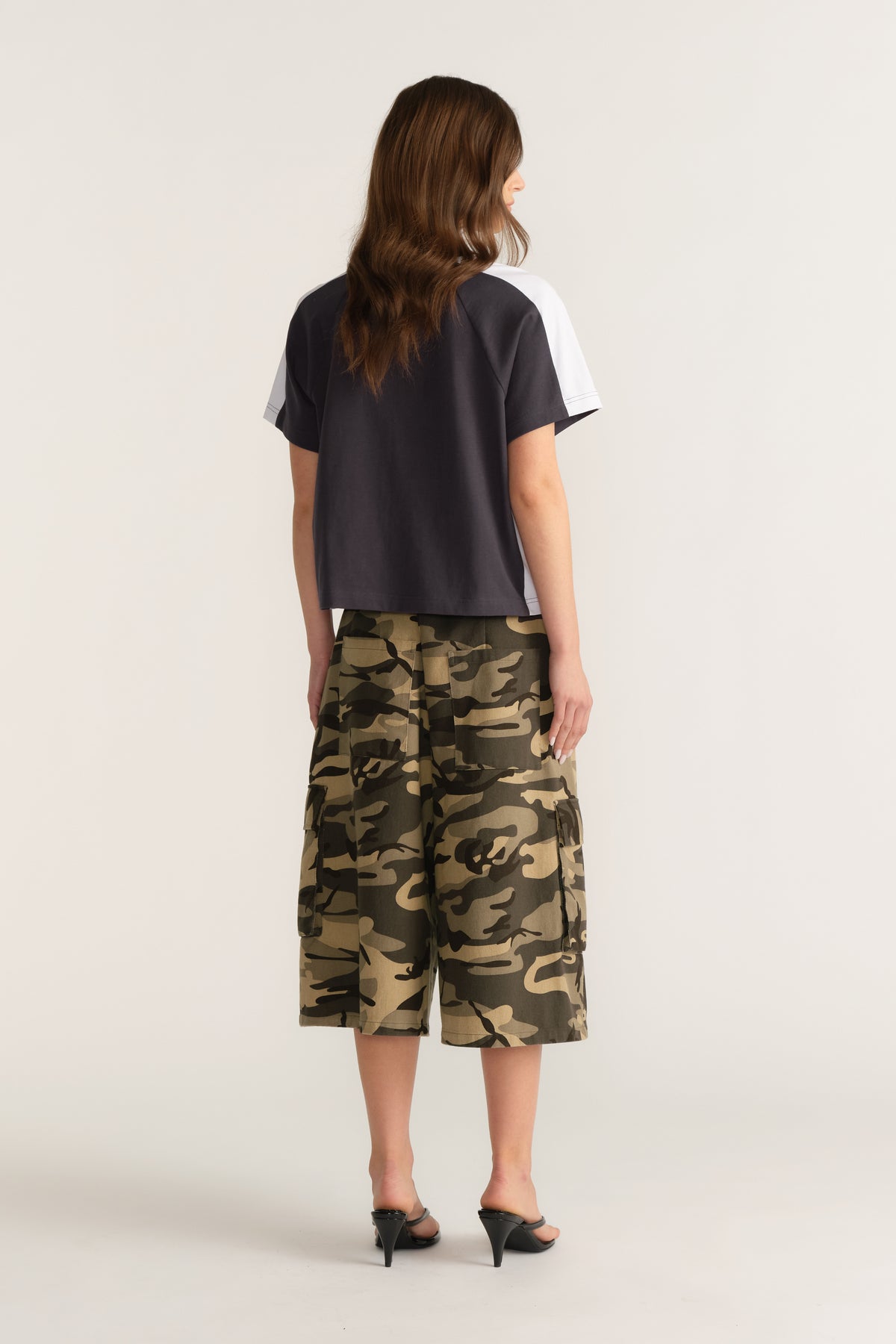 Back view of a woman wearing a dark contrast sleeve tee with camouflage cargo shorts