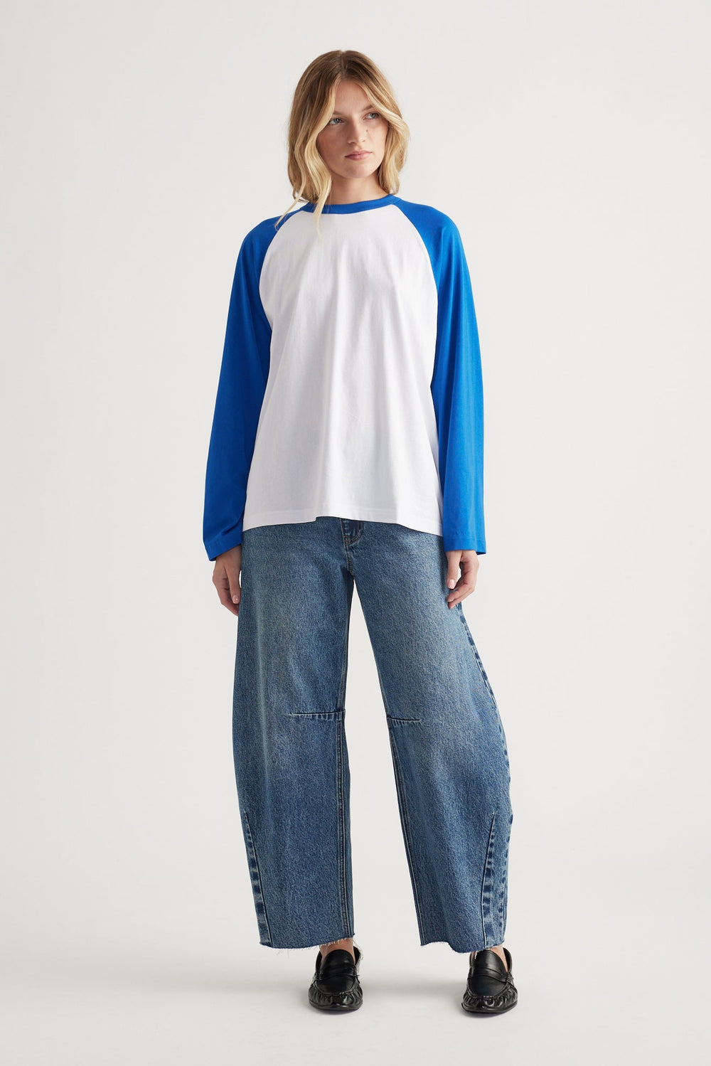 Woman wearing a relaxed-fit long sleeve tee with cobalt blue raglan sleeves paired with wide-leg denim jeans and black shoes