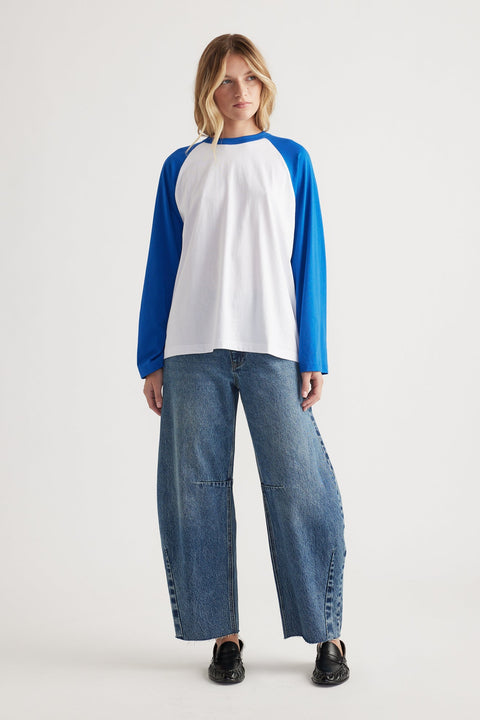 Woman wearing a relaxed-fit long sleeve tee with cobalt blue raglan sleeves paired with wide-leg denim jeans and black shoes
