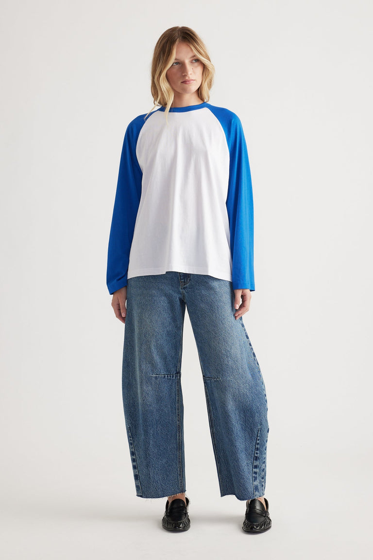 Woman wearing a relaxed-fit long sleeve tee with cobalt blue raglan sleeves paired with wide-leg denim jeans and black shoes