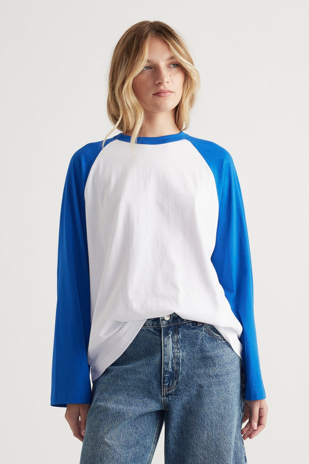 Woman wearing a relaxed fit long sleeve raglan tee in white with cobalt blue sleeves paired with casual denim jeans