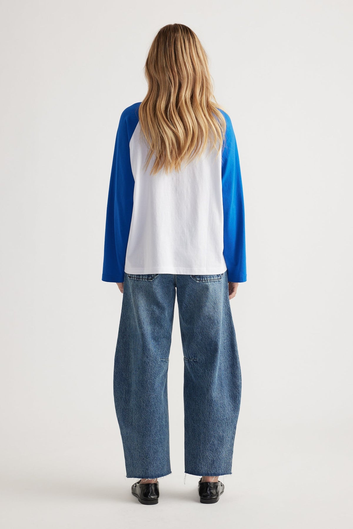 Woman wearing relaxed fit blue sleeve raglan tee paired with loose straight leg jeans and black slip-on shoes