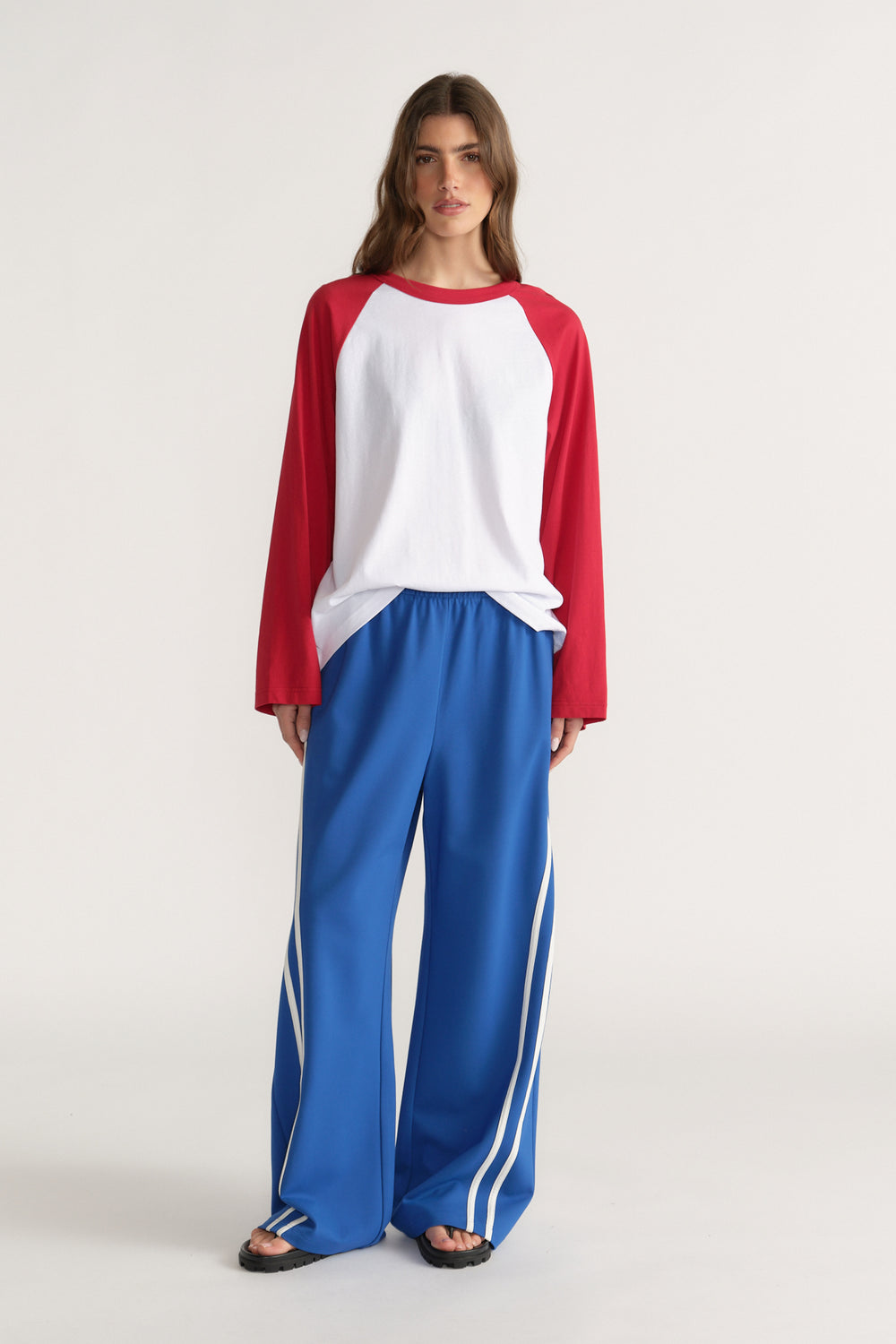Woman wearing a white and red raglan long sleeve tee with blue wide leg track pants and sandals