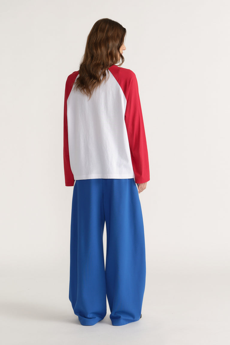 Woman seen from behind wearing a white tee with red raglan sleeves and flowing blue wide leg pants