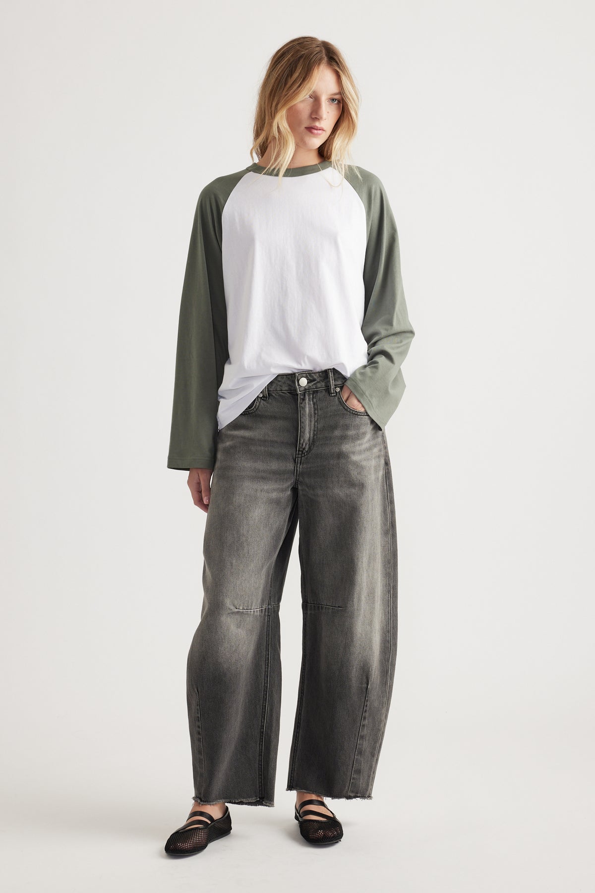 Woman wearing white and olive raglan sleeve long sleeve tee with loose faded black wide-leg jeans and black flats